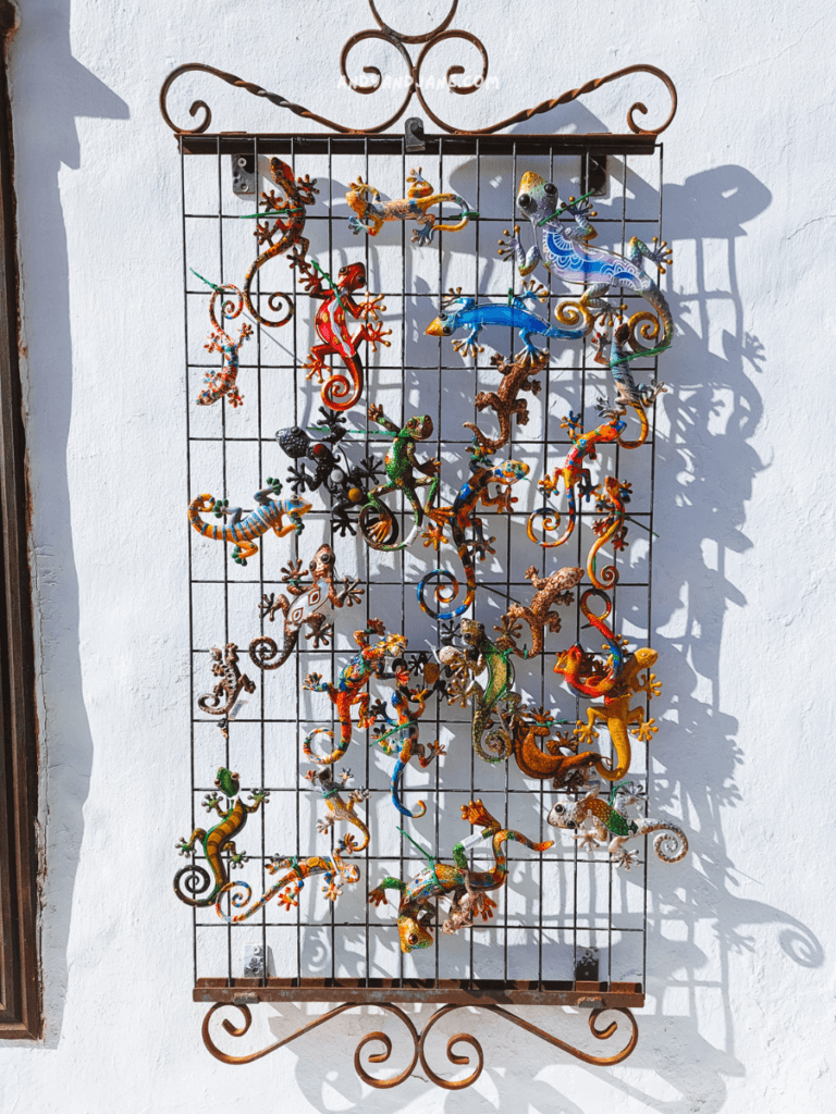 A colorful metal art display of lizards and chameleons hangs on a white wall, casting intricate shadows below.