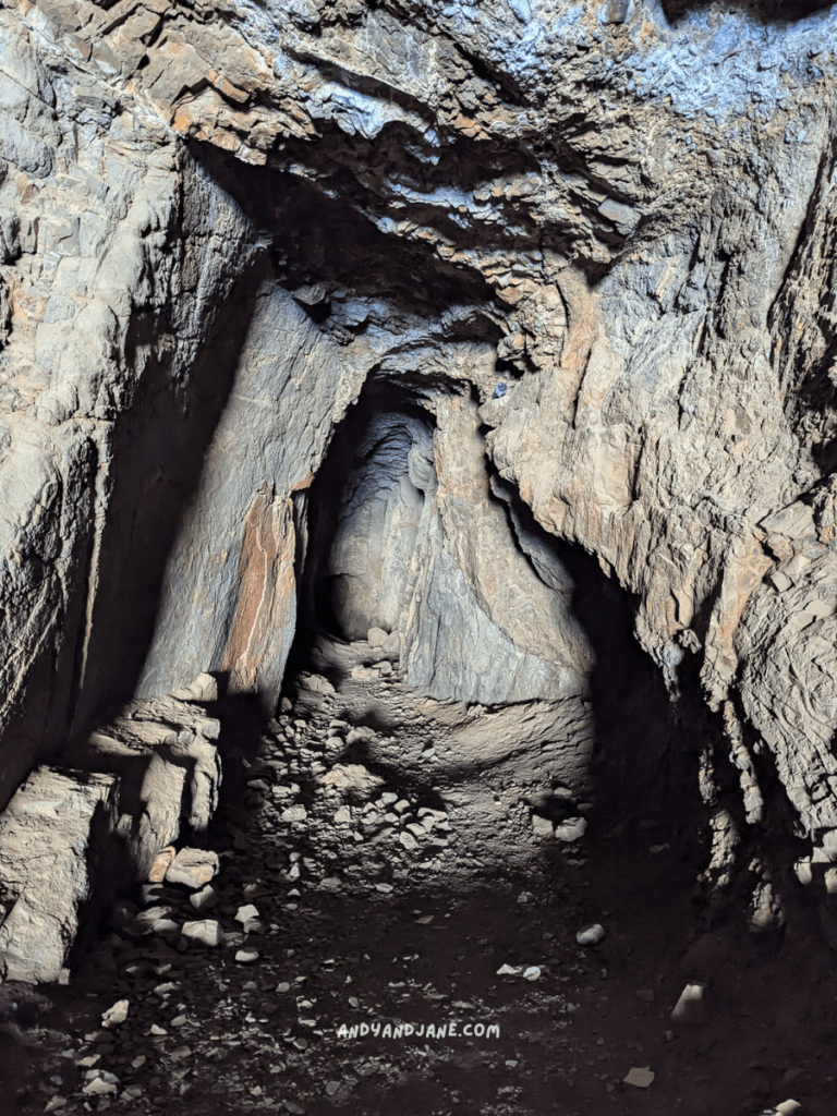 A dark, rocky cave at Ajuy with jagged walls and a narrow passageway leading deeper into the earth, scattered with stones.