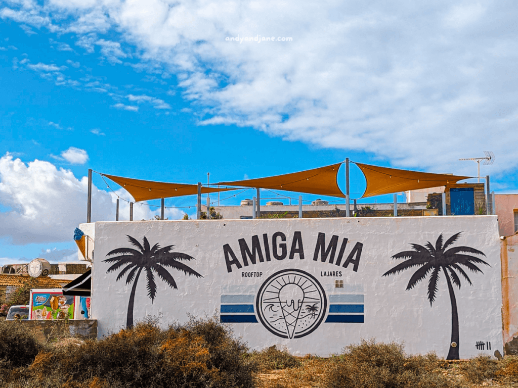 Rooftop bar "Amiga Mia" in Lajares, featuring a palm tree mural and a sunny sky, with a vibrant atmosphere and outdoor seating.