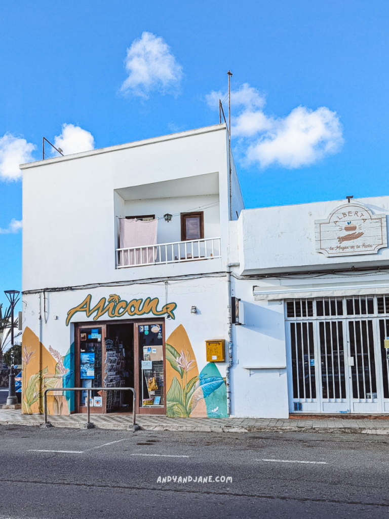 A vibrant storefront named "African" adorned with tropical murals, set against a blue sky and a neighboring white building in Lajares.