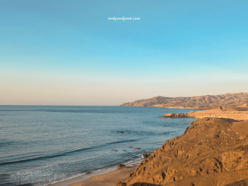 Stunning coastal view at sunset in La Pared, Fuerteventura - showcasing rocky cliffs, gentle waves, and distant mountains under a clear blue sky.