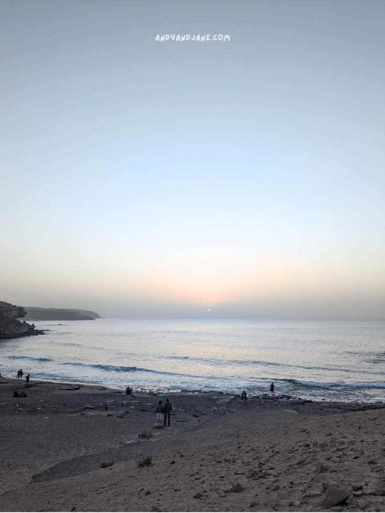 Sunset view over a calm beach in La Pared, with silhouettes of people enjoying the shore and gentle waves under a soft pastel sky.