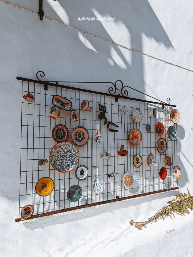 A decorative metal grid displays colorful ceramic plates and pottery against a light blue wall, casting intriguing shadows.