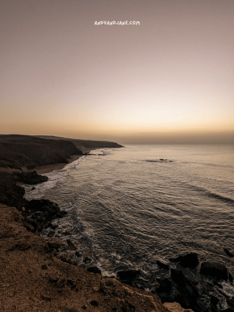 A serene coastal view at dusk, featuring waves gently lapping at the rugged shore under a gradient sky at Playa de La Pared.