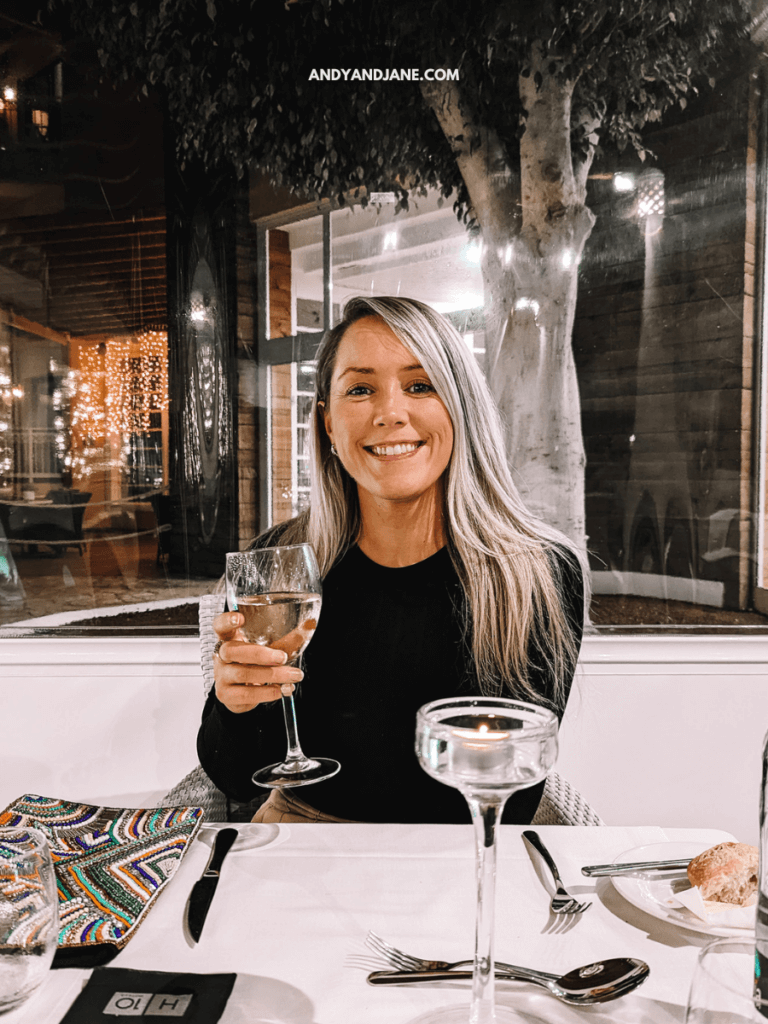 A woman with long blonde hair holds a large drink at a dinner table adorned with decorative napkins and a lit candle.